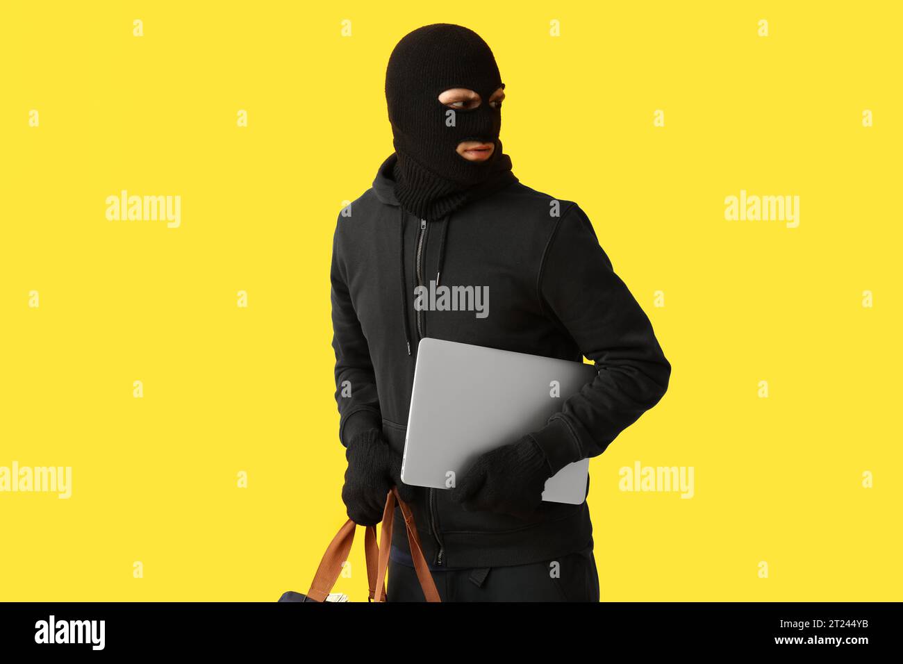 Male thief with laptop on yellow background Stock Photo - Alamy