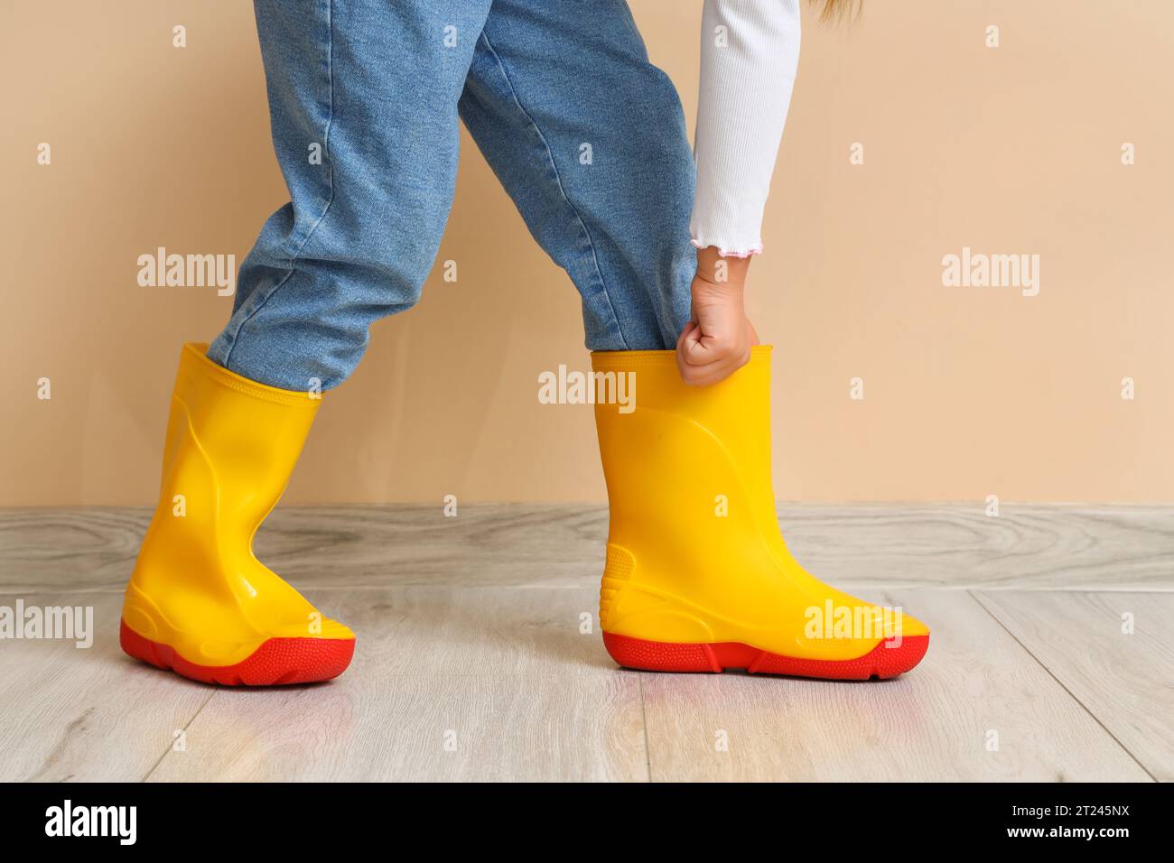 Little girl in rubber boots near beige wall, closeup Stock Photo - Alamy