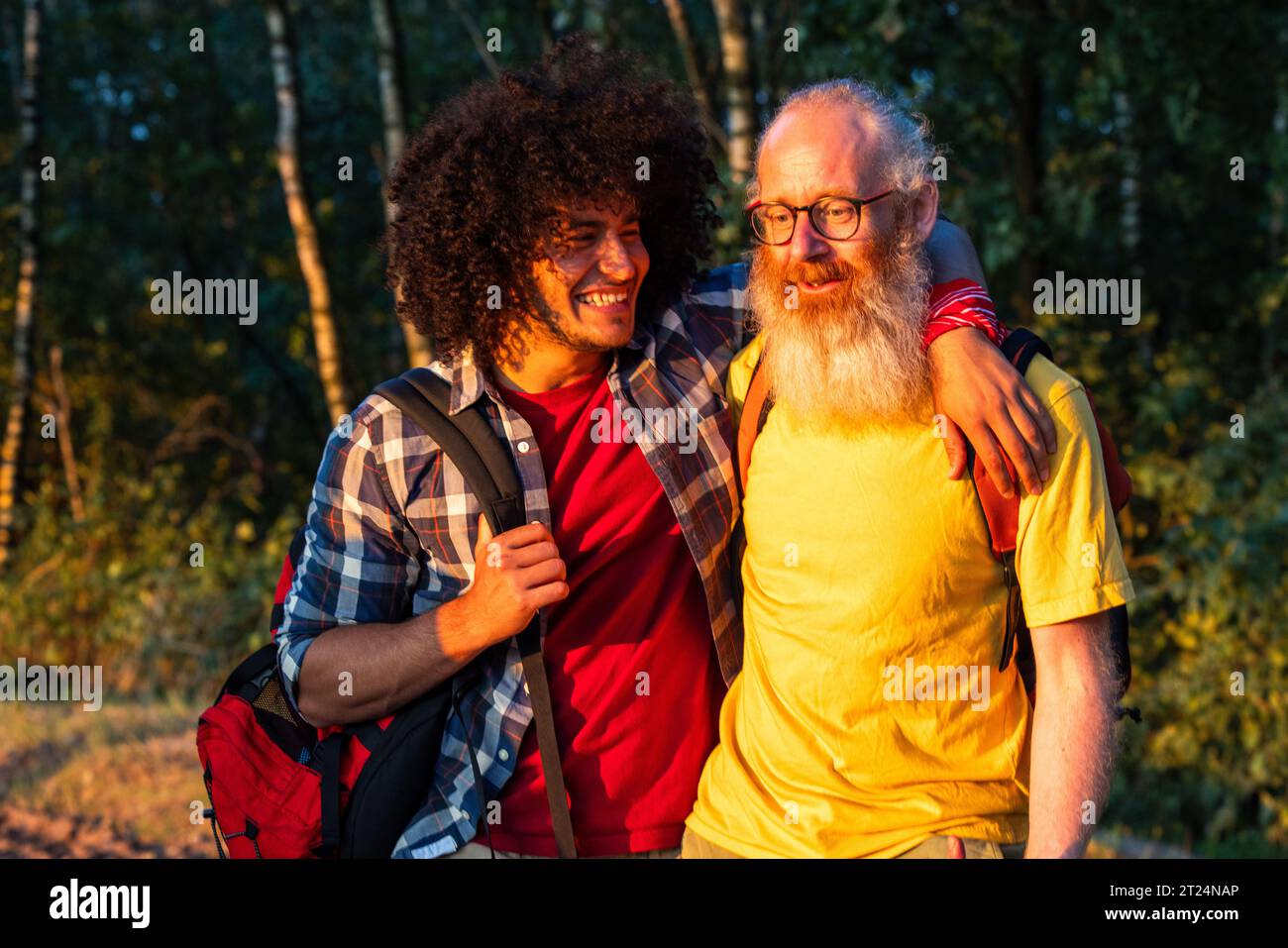 A heartwarming moment captured as a father and son share a loving hug while on a bonding hiking trip in the serene beauty of nature, bathed in the warm glow of the setting sun. Father and Son Hiking in Golden Sunset. High quality photo Stock Photo