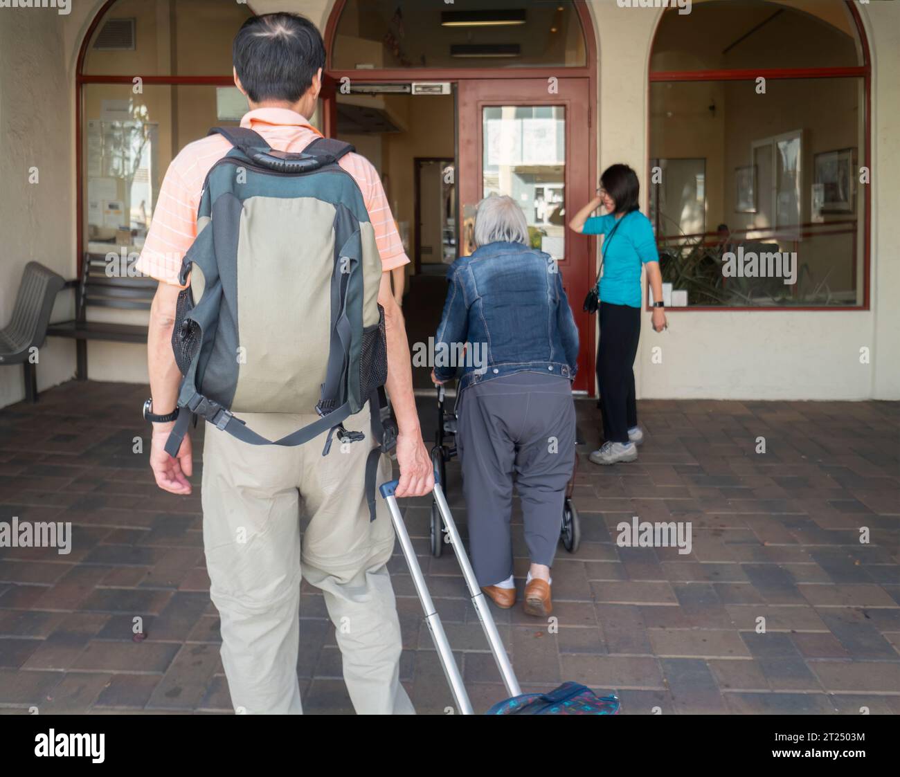 Senior woman with a mobility walker returning home at retirement village from a holiday trip, accompanied by son and daughter. Stock Photo