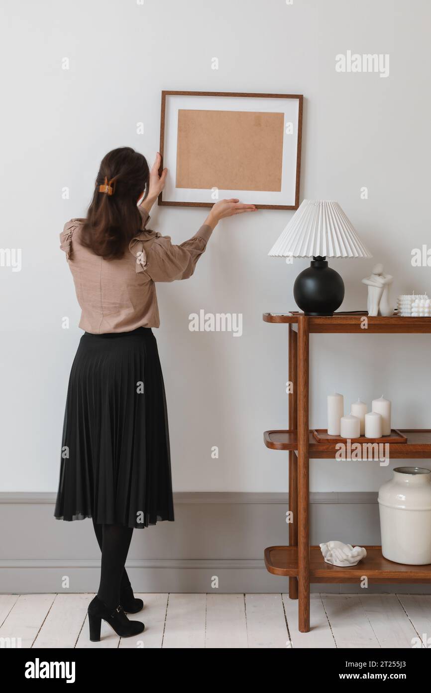 Rear view of an elegant woman deciding where to hang a picture frame Stock Photo