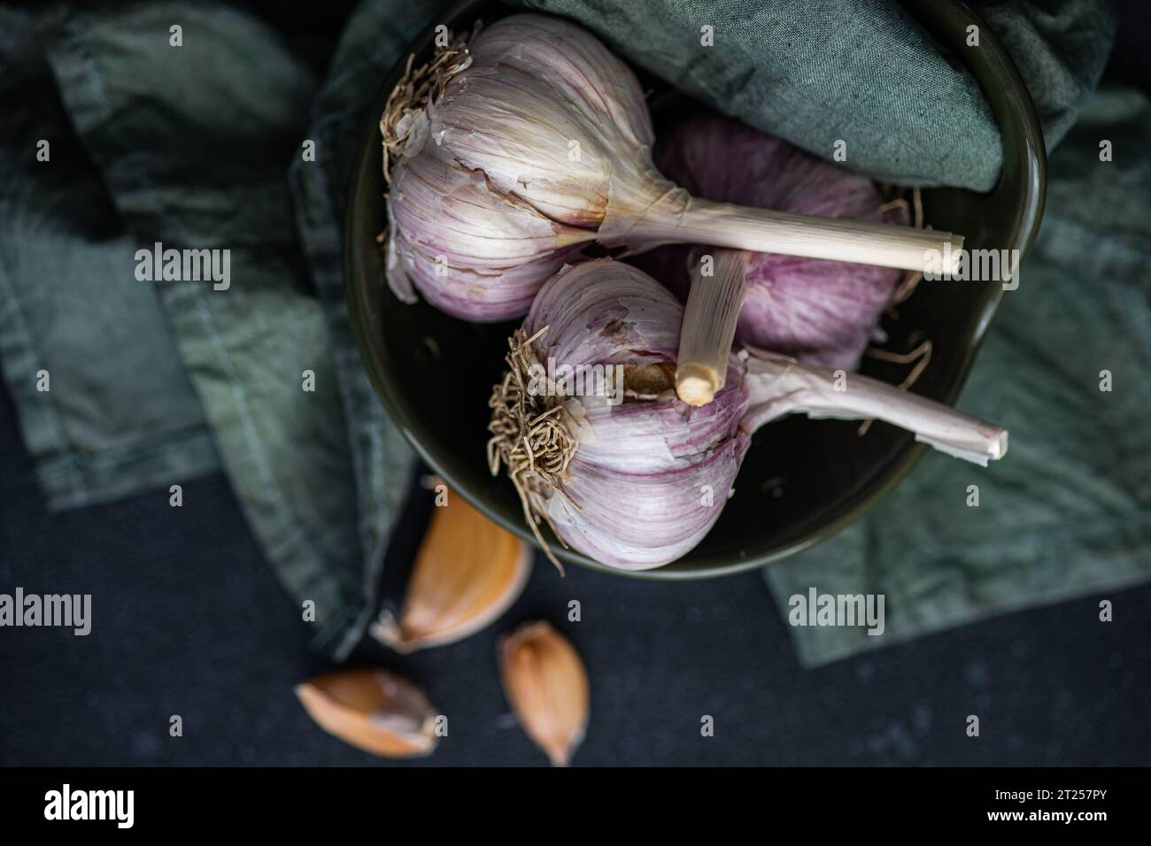 Overhead view of fresh garlic bulbs and cloves in a bowl with a napkin Stock Photo