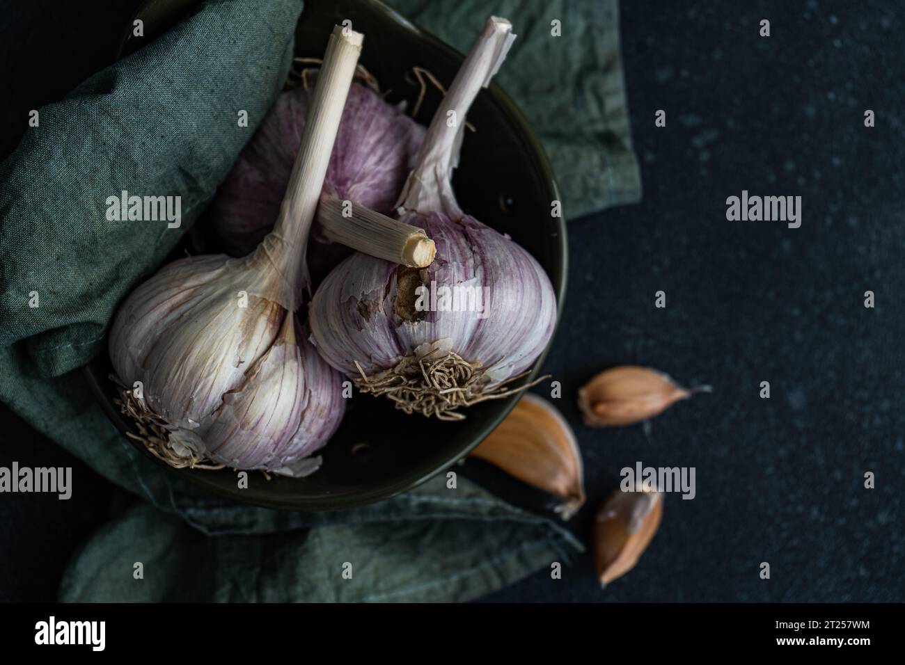 Overhead view of fresh garlic bulbs and cloves in a bowl with a napkin Stock Photo