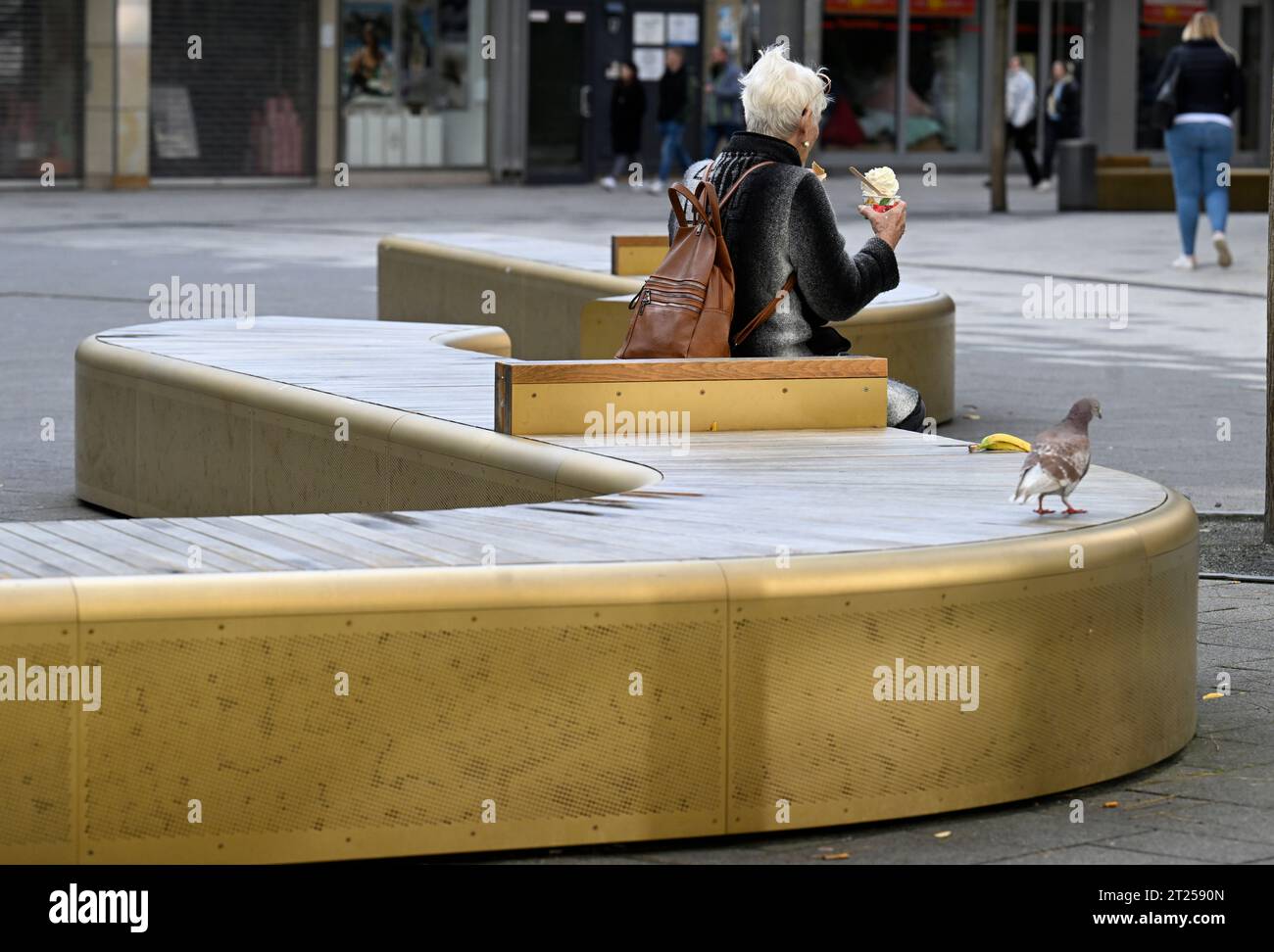 Wuppertal, Germany. 16th Oct, 2023. A woman sits on the shiny gold benches in the pedestrian zone of Elberfeld. In its 51st Black Book, the Taxpayers' Association has listed 100 exemplary cases nationwide which, according to its research, represent a waste of taxpayers' money. The enumeration presented on Tuesday nearly 200 sides strong contains also 13 cases from North Rhine-Westphalia. Among the most astonishing examples are uncomfortable but golden benches in Wuppertal's city center. Credit: Roberto Pfeil/dpa/Alamy Live News Stock Photo
