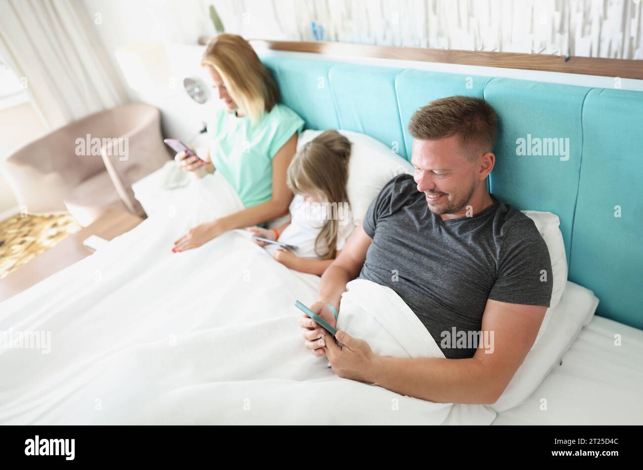 Close-up of family stare in smartphone, morning in bed with devices, kill time. People addicted to modern technologies, bored. Social media, addict co Stock Photo