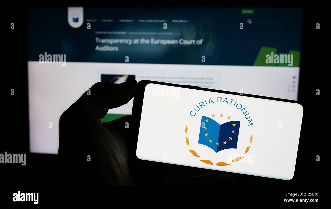 Person holding mobile phone with logo of EU institution European Court of Auditors (ECA) in front of web page. Focus on phone display. Stock Photo