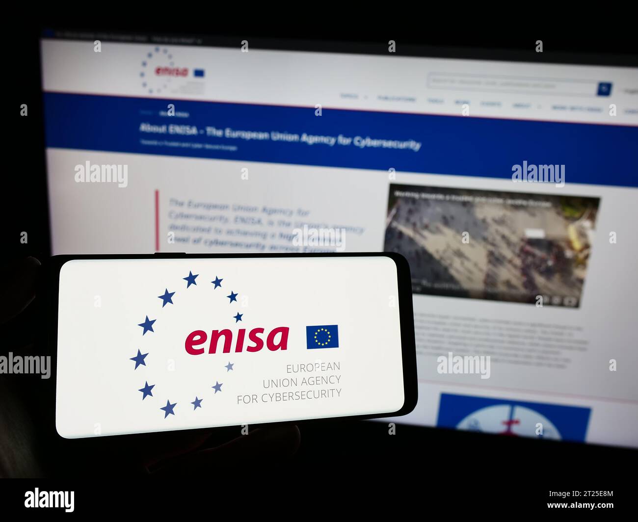 Person holding mobile phone with logo of European Union Agency for Cybersecurity (ENISA) in front of web page. Focus on phone display. Stock Photo