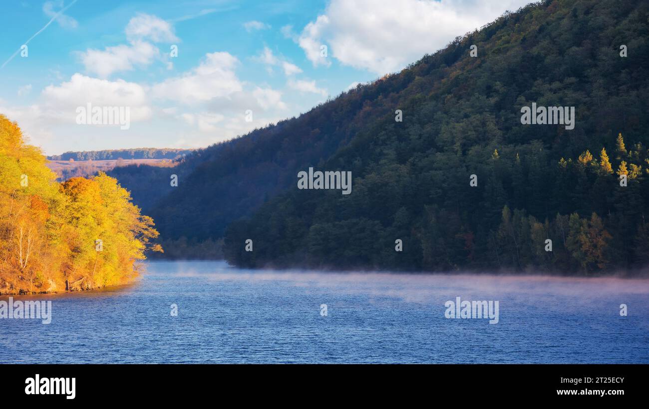 countryside scenery by lake in fall season. scenery with forested mountains in vivid autumn colors. warm sunny weather with clouds on the sky Stock Photo