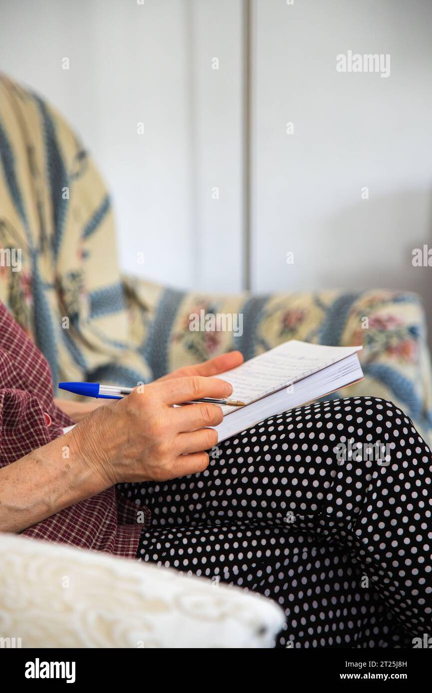 Close up of a person writing on a notebook. Adult person sitting on a sofa writing a text with an ink pen and in a notebook. Stock Photo