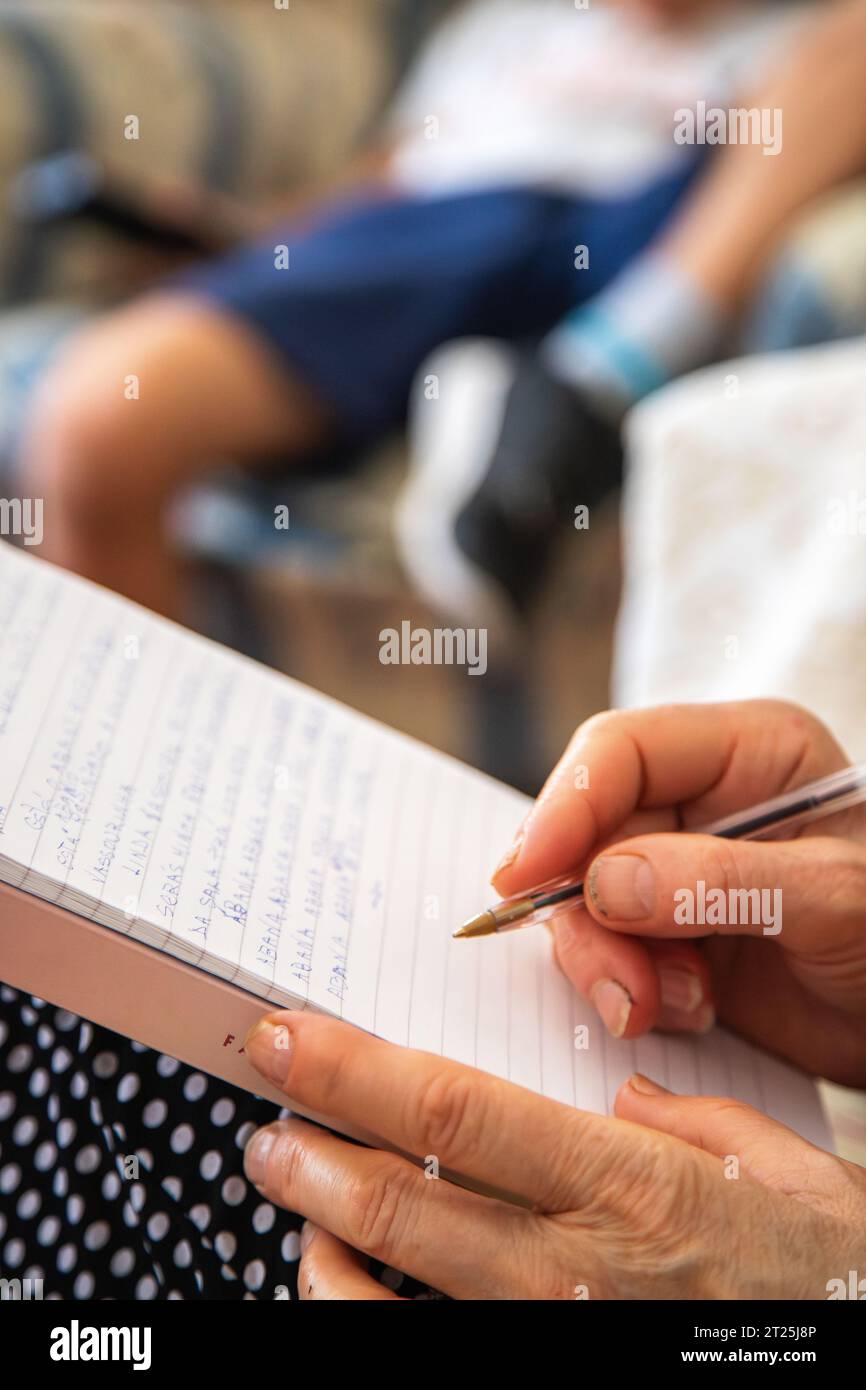 Close up of a person writing on a notebook. Adult person sitting on a sofa writing a text with an ink pen and in a notebook. Stock Photo