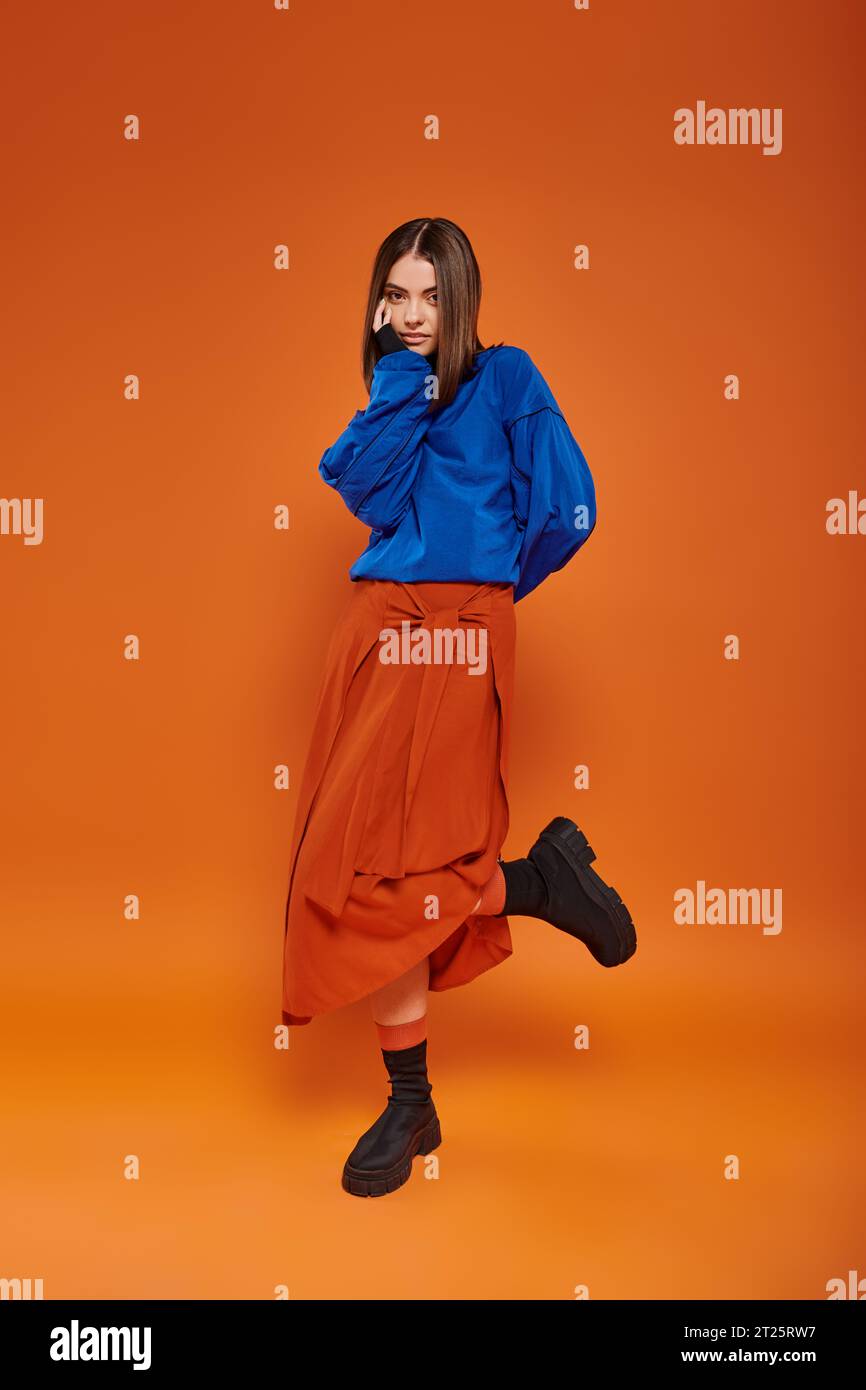 fashionable and young woman with pierced nose standing in autumn skirt and boots on orange backdrop Stock Photo