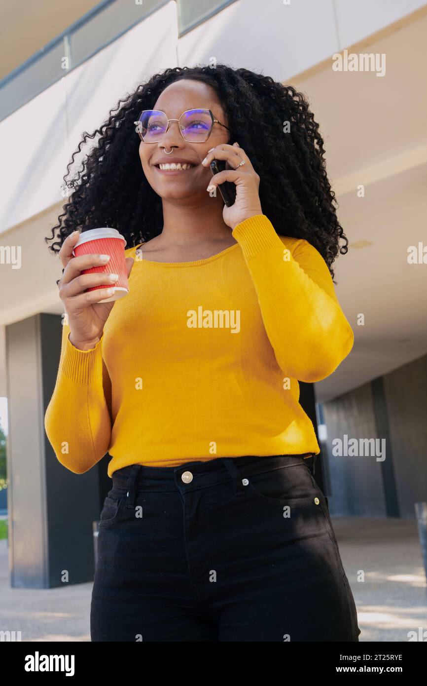 Young smiling black woman at mobile phone while drinking coffee. Stock Photo