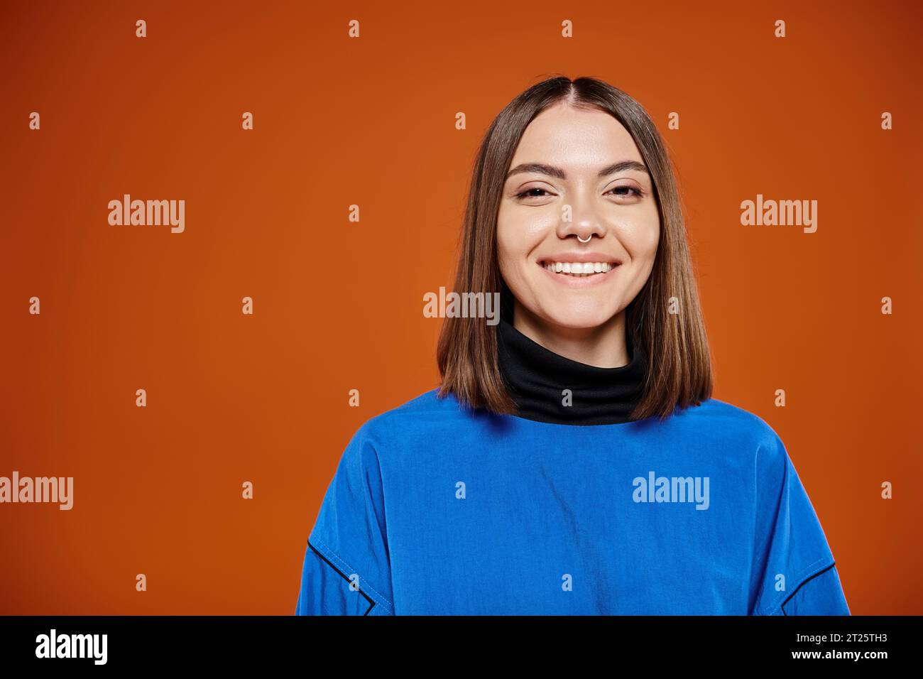 attractive smiley woman in casual blue jacket smiling cheerfully at camera on orange background Stock Photo