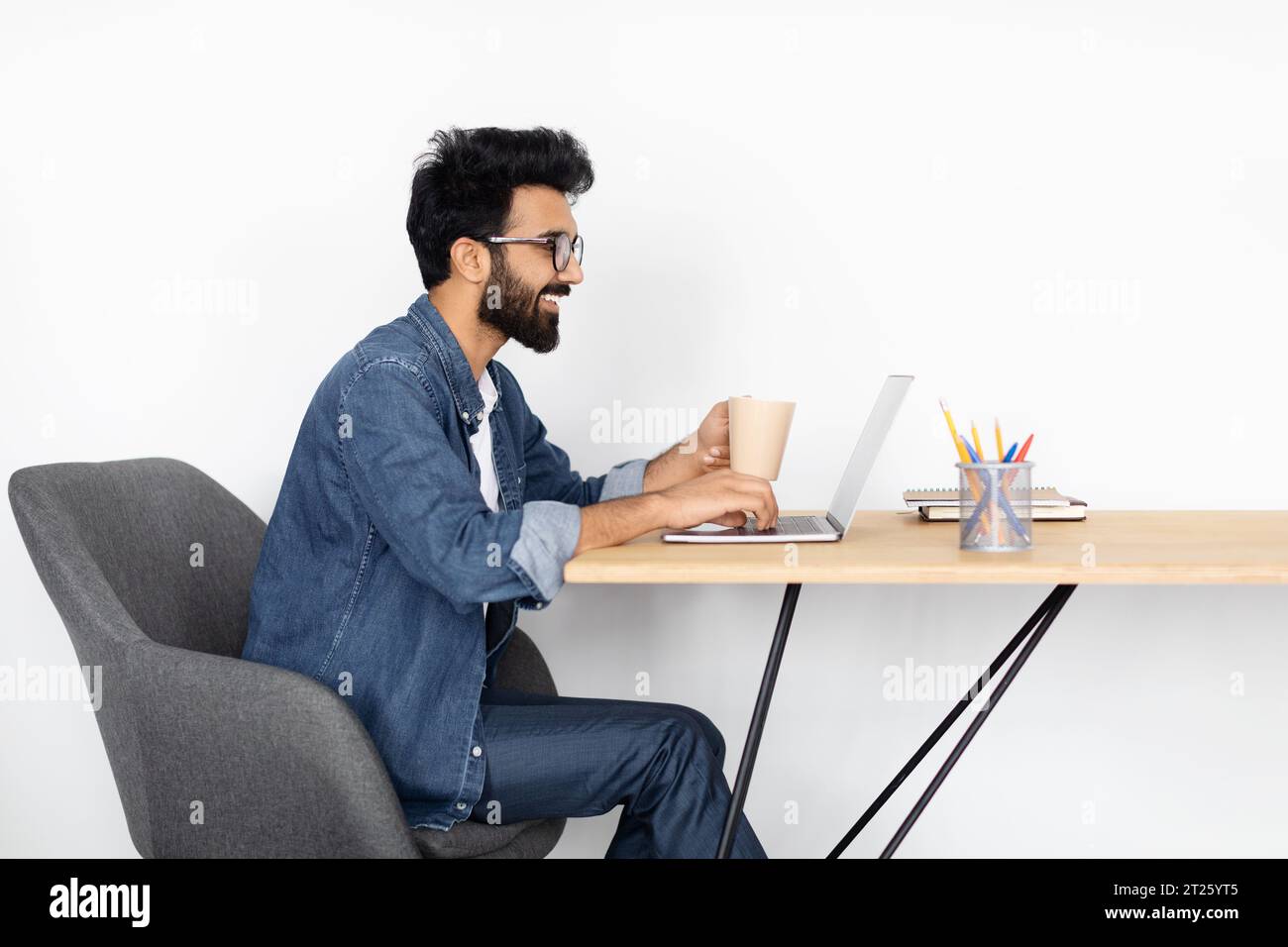 Focused Indian Freelancer Using Laptop at Table Stock Photo