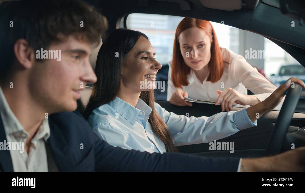 Caucasian seller woman female automobile salon manager trader saleswoman consult clients helping explain trade new car to happy couple buyers Stock Photo