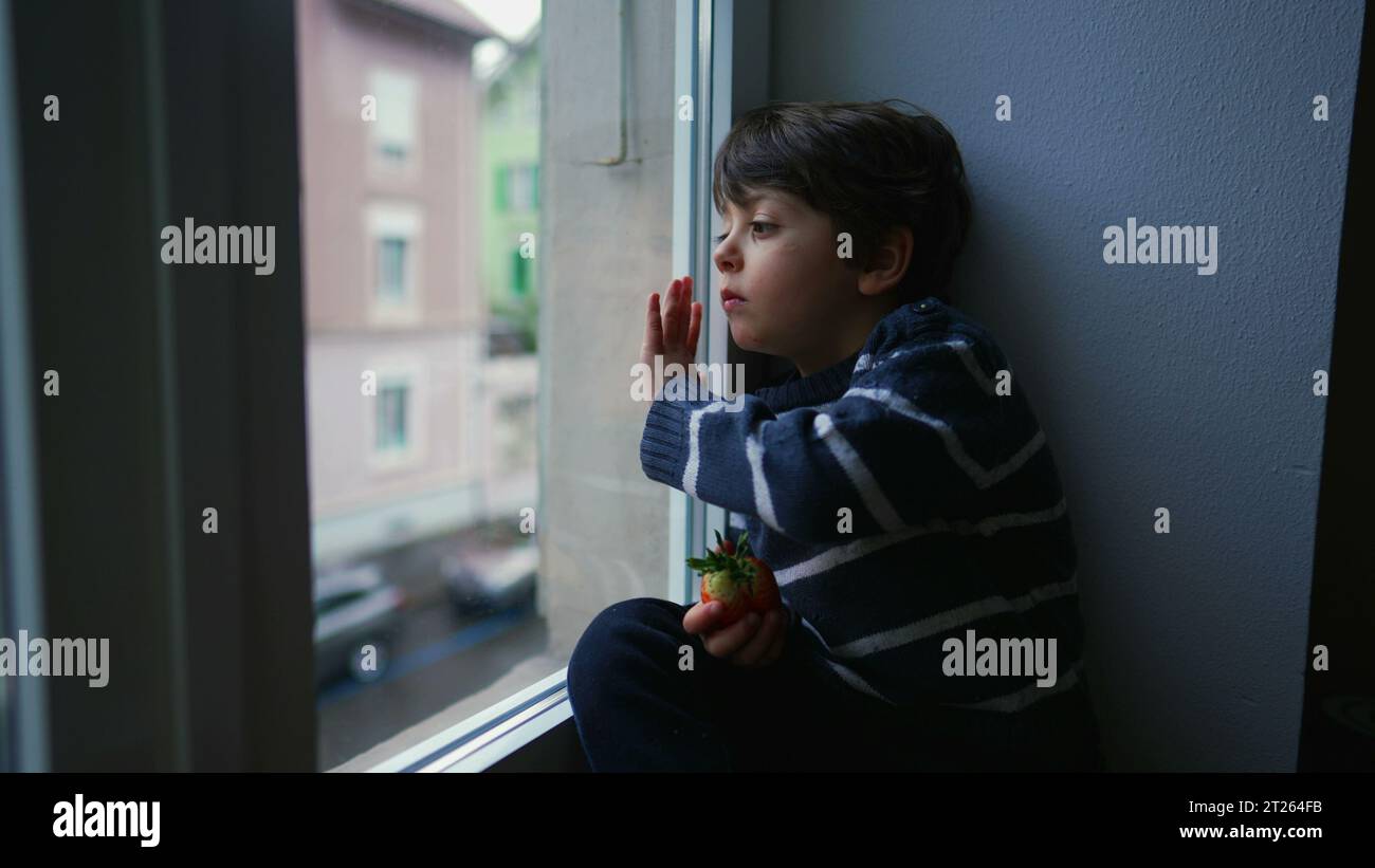 Melancholy Little Boy Staring at View from Window, Wanting to Go Out but Stuck at Home in Sad Bored Emotion Stock Photo