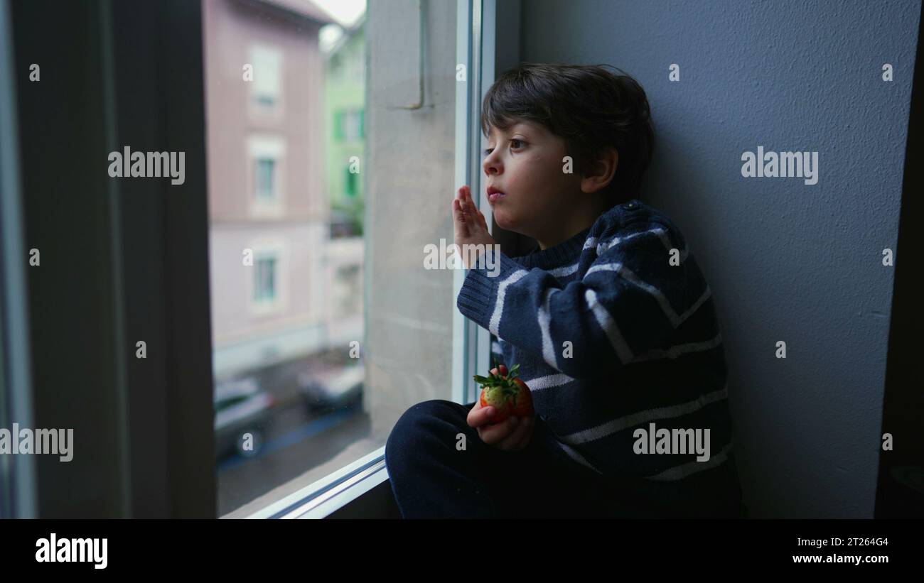 Melancholy Little Boy Staring at View from Window, Wanting to Go Out but Stuck at Home in Sad Bored Emotion Stock Photo