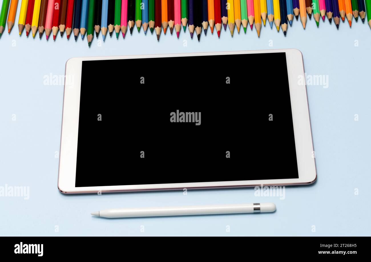 A tablet, stylus, and colored pencils lie on the table. View from the top. High quality photo. The concept of online education, training, private draw Stock Photo