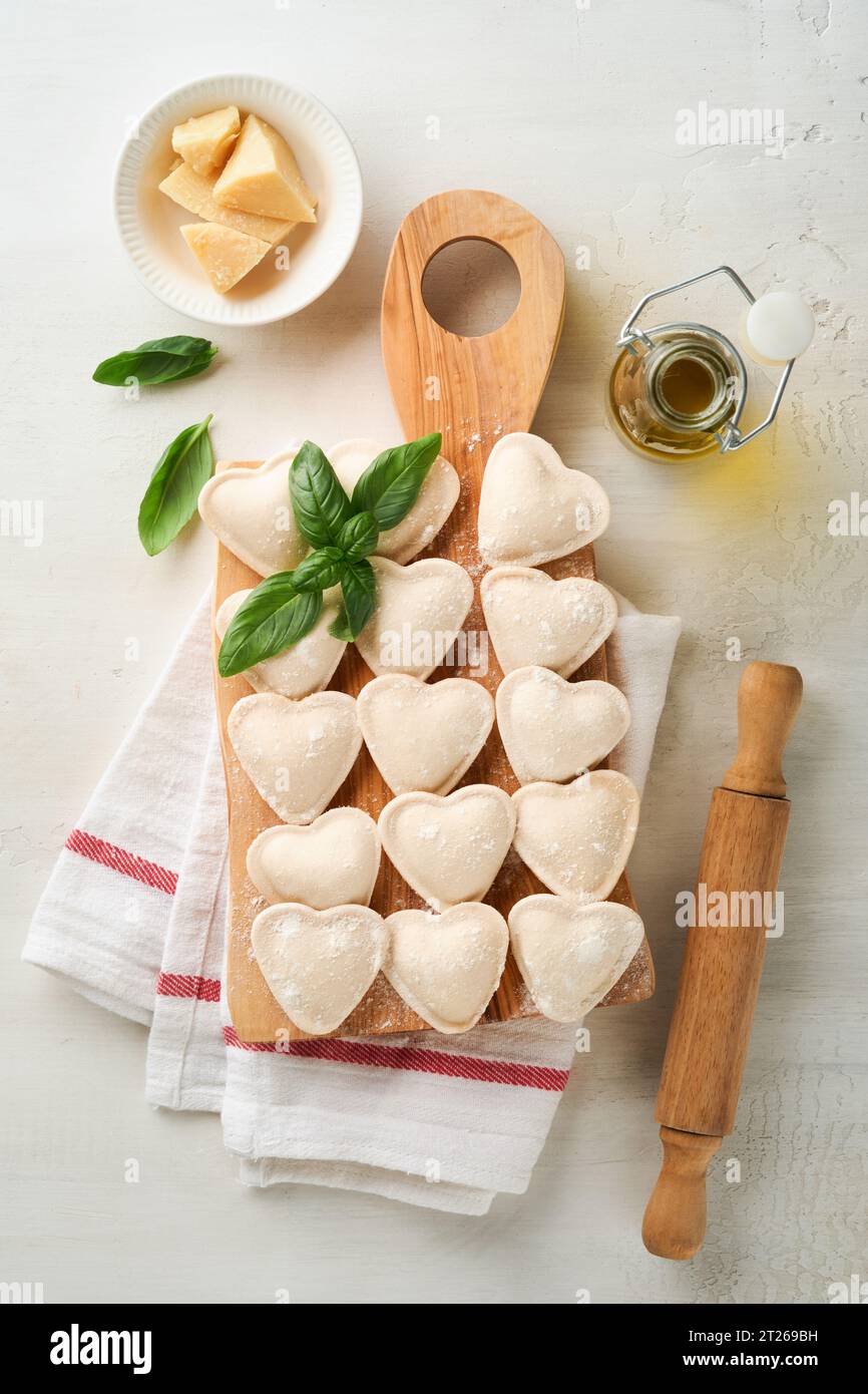 Italian ravioli pasta in heart shape. Tasty raw ravioli with flour and basil on white background. Food cooking ingredients background. Valentines or M Stock Photo