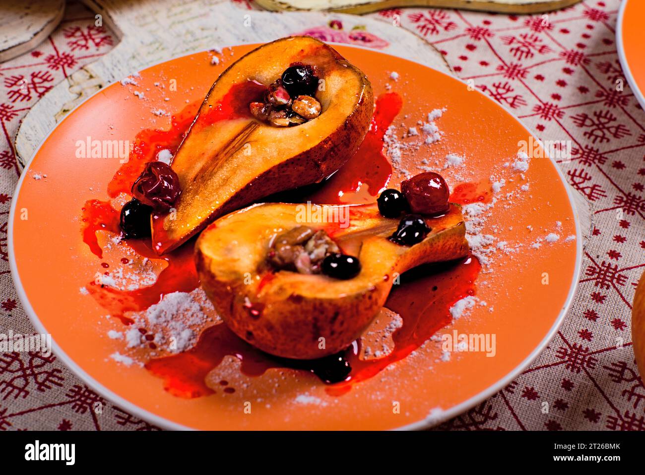 Cooked pear with berry sauce on orange plate. Stock Photo