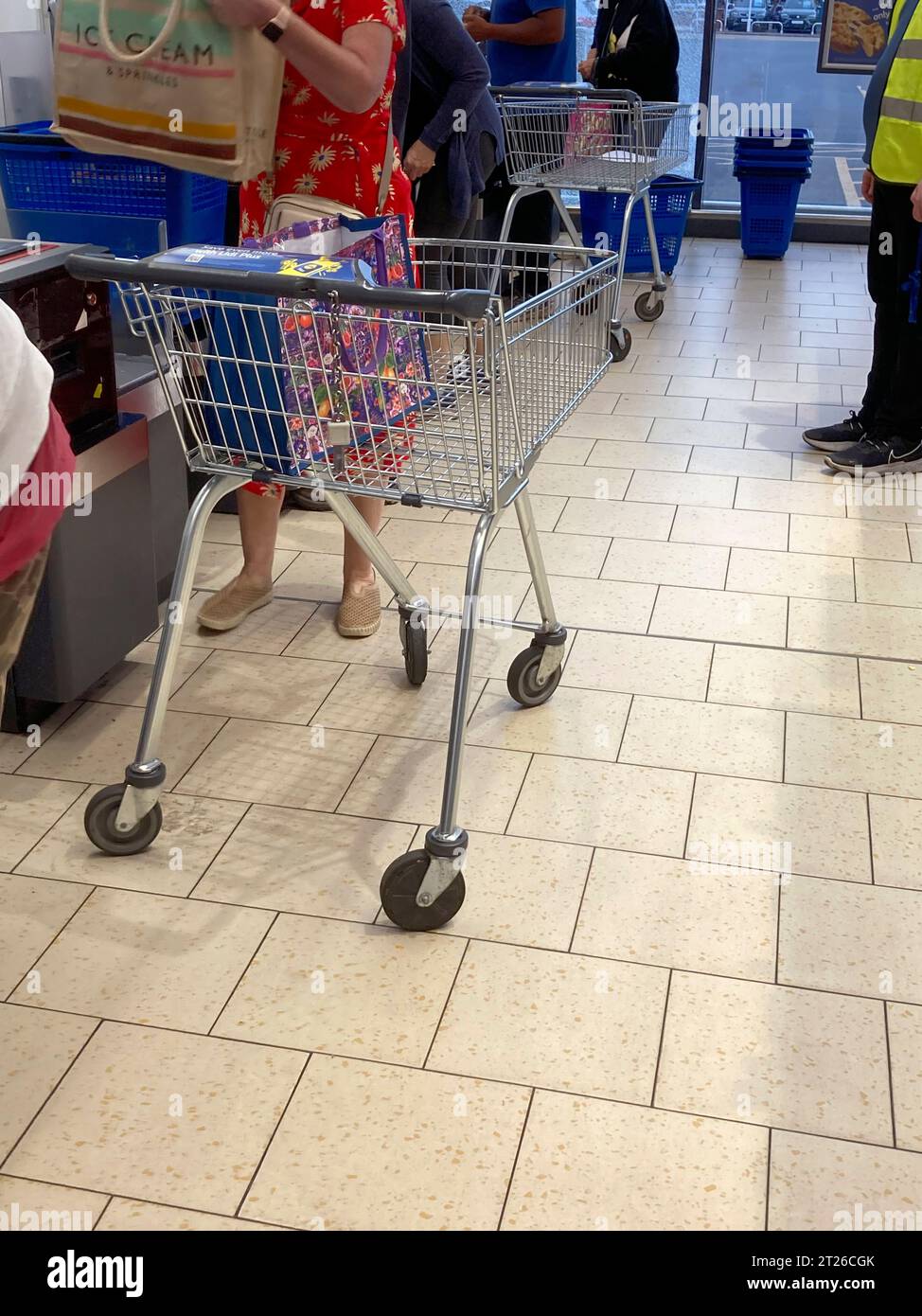 Customers with trolly / trolley / trollies pay at the self service checkout / check out tills (meant for basket use) at a Lidl supermarket. UK. (135) Stock Photo
