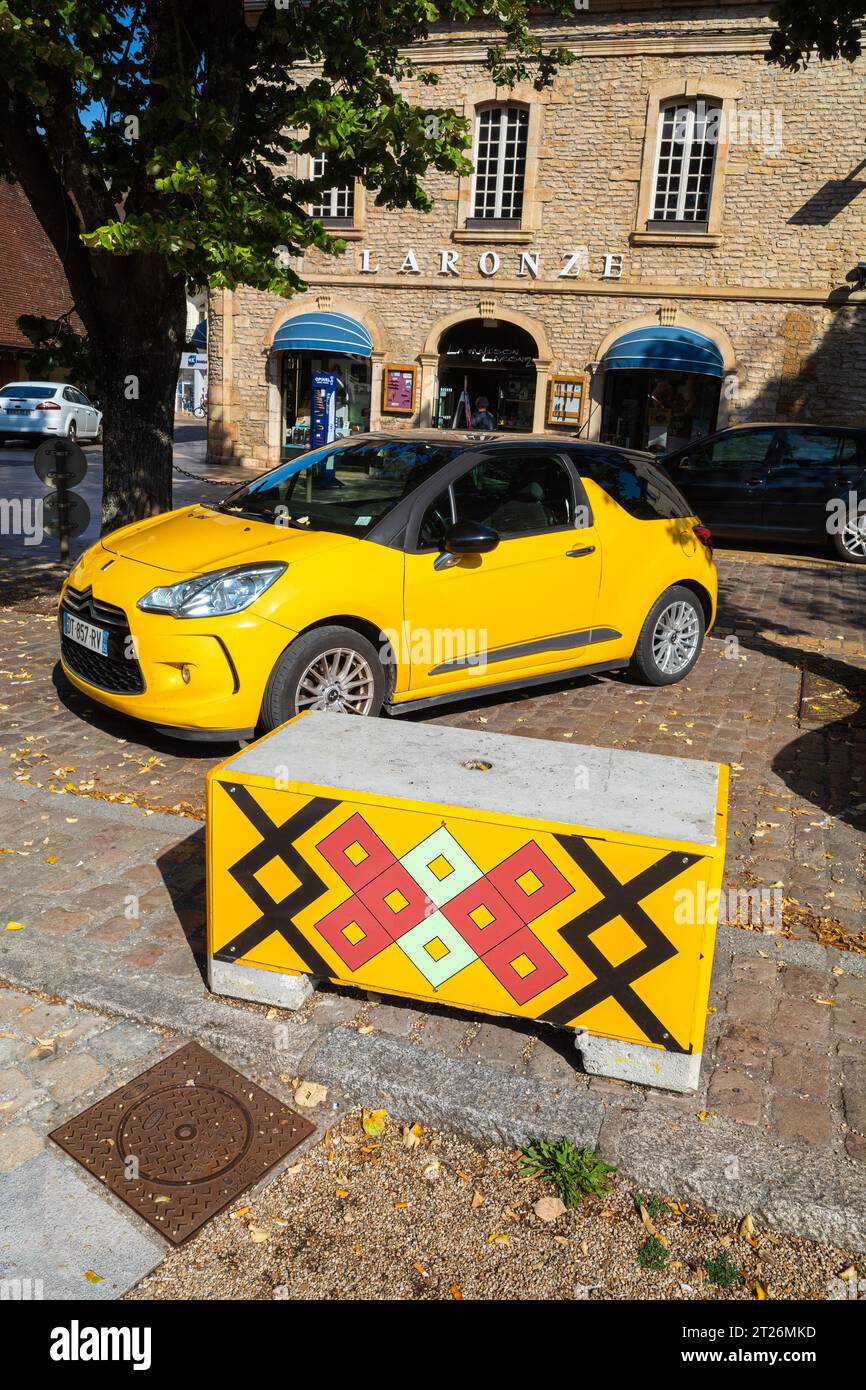 Beaune, France - August 16, 2023: A yellow Citroen car in front of a kind of box bearing a pattern from the roof of the famous Beaune hospice Stock Photo