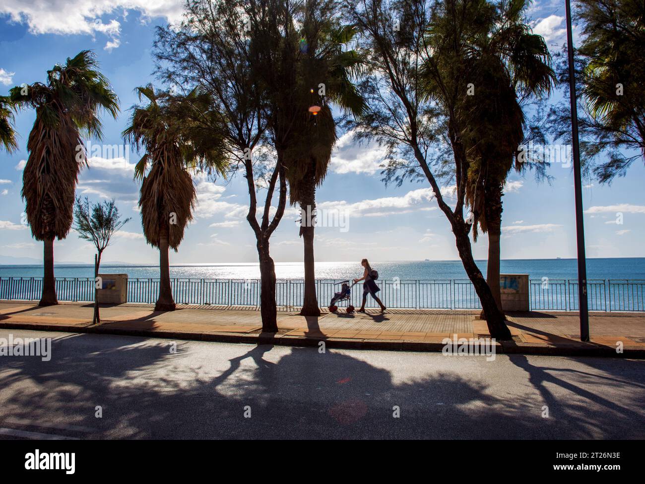 Awe view of embankment with motion blurred people   (woman with child in stroll) in Salerno. Palm alley amd Mediterranean Sea behind Stock Photo