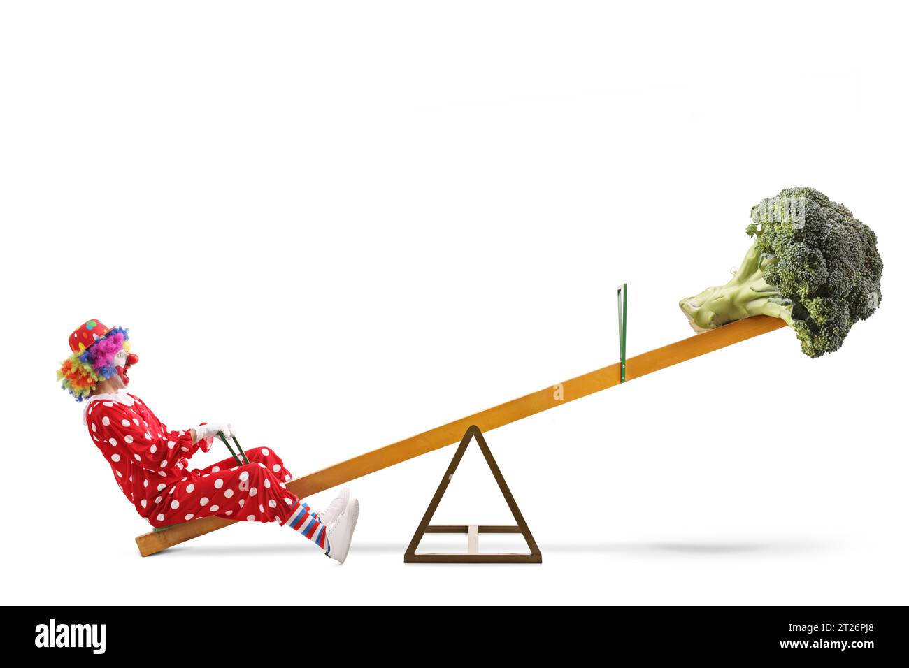 Clown with a broccoli vegetable on a seesaw, healthy diet concept isolated on white background Stock Photo