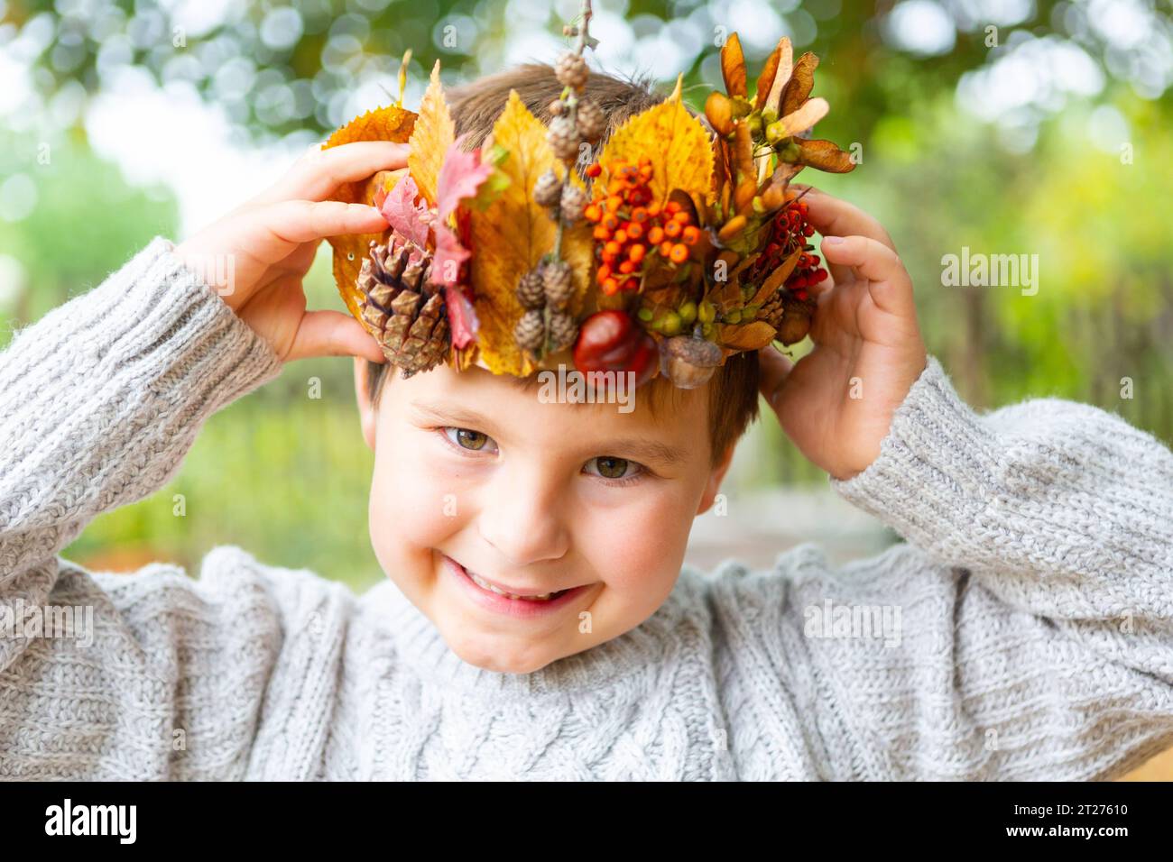 7 October 2023: Little boy is happy with self-made crown made of colorful leaves and pine cones. Child with autumn crown on his head in the garden. Playing and crafting concept *** Kleiner Junge freut sich über eine selbst gebastelte Krone aus bunten Blättern und Tannenzapfen. Kind mit Herbst Krone auf dem Kopf im Garten. Spielen und Basteln Konzept Credit: Imago/Alamy Live News Stock Photo