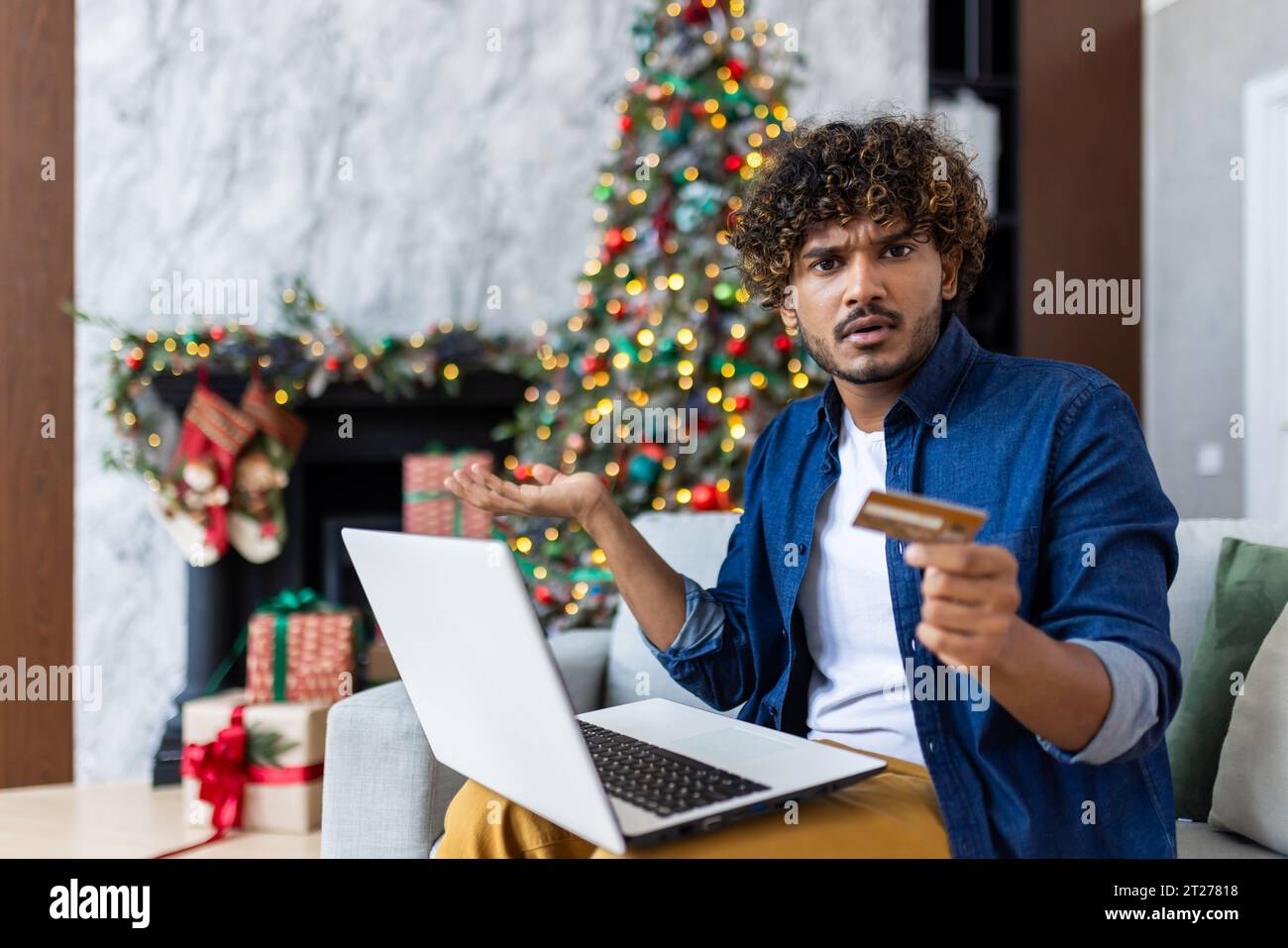 Portrait of cheated unsatisfied man at home on New Year and Christmas holidays, hispanic man looking at camera with laptop rejected money transfer, using bank credit card. Stock Photo