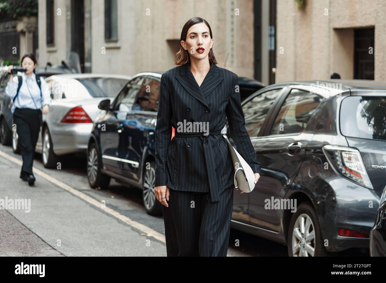 A guest wears black striped pantsuit, white bag, seen outside MAX MARA