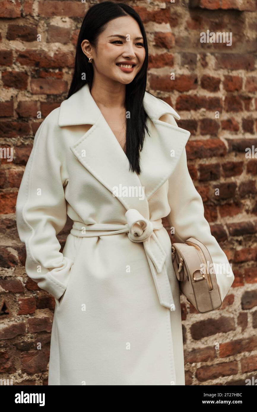 A guest wears white coat, beige bag, seen outside MAX MARA show during