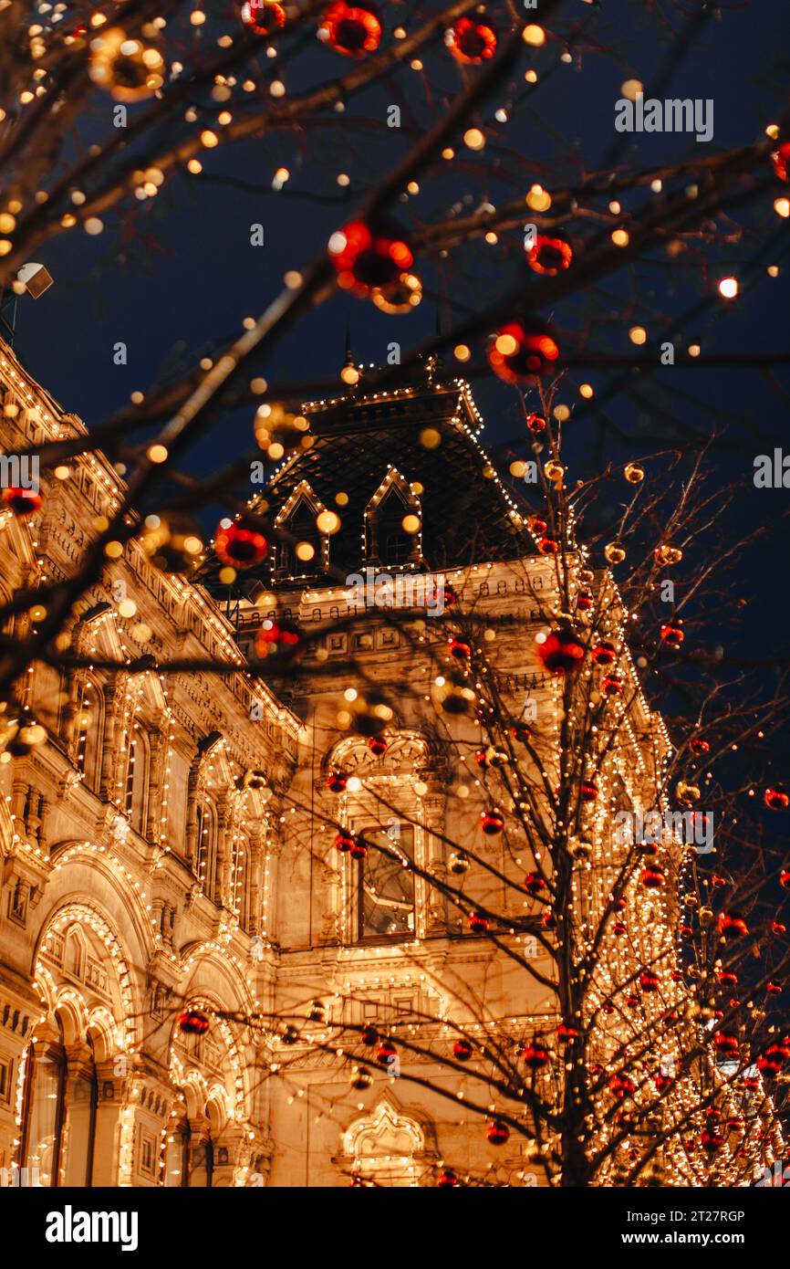 Dried tree branches decorated with red and gold Christmas balls. New Year outdoor decorations against a glowing golden building. Vertical festive post Stock Photo