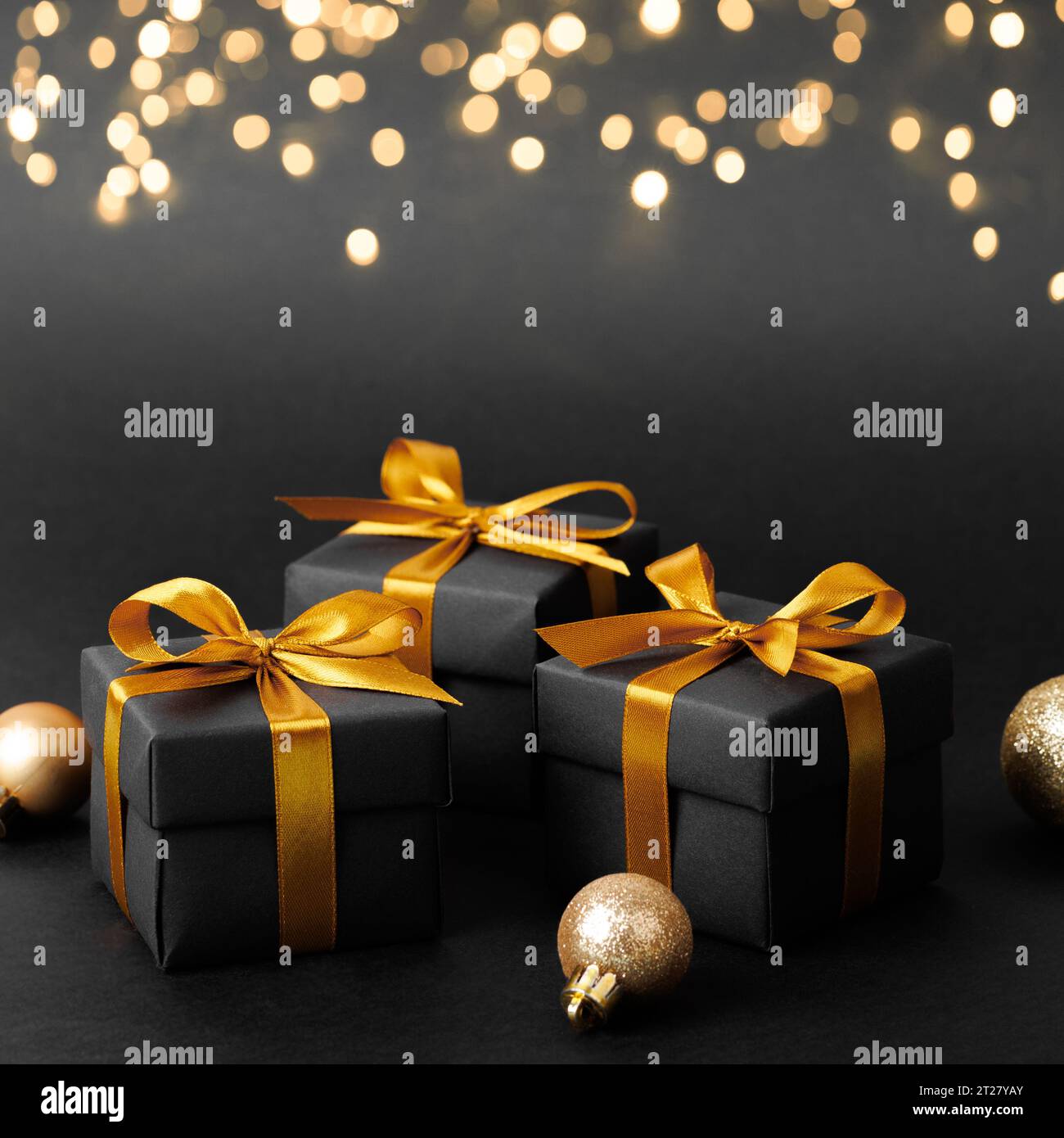 Black gift box with golden ribbon bow on black background. Stock Photo