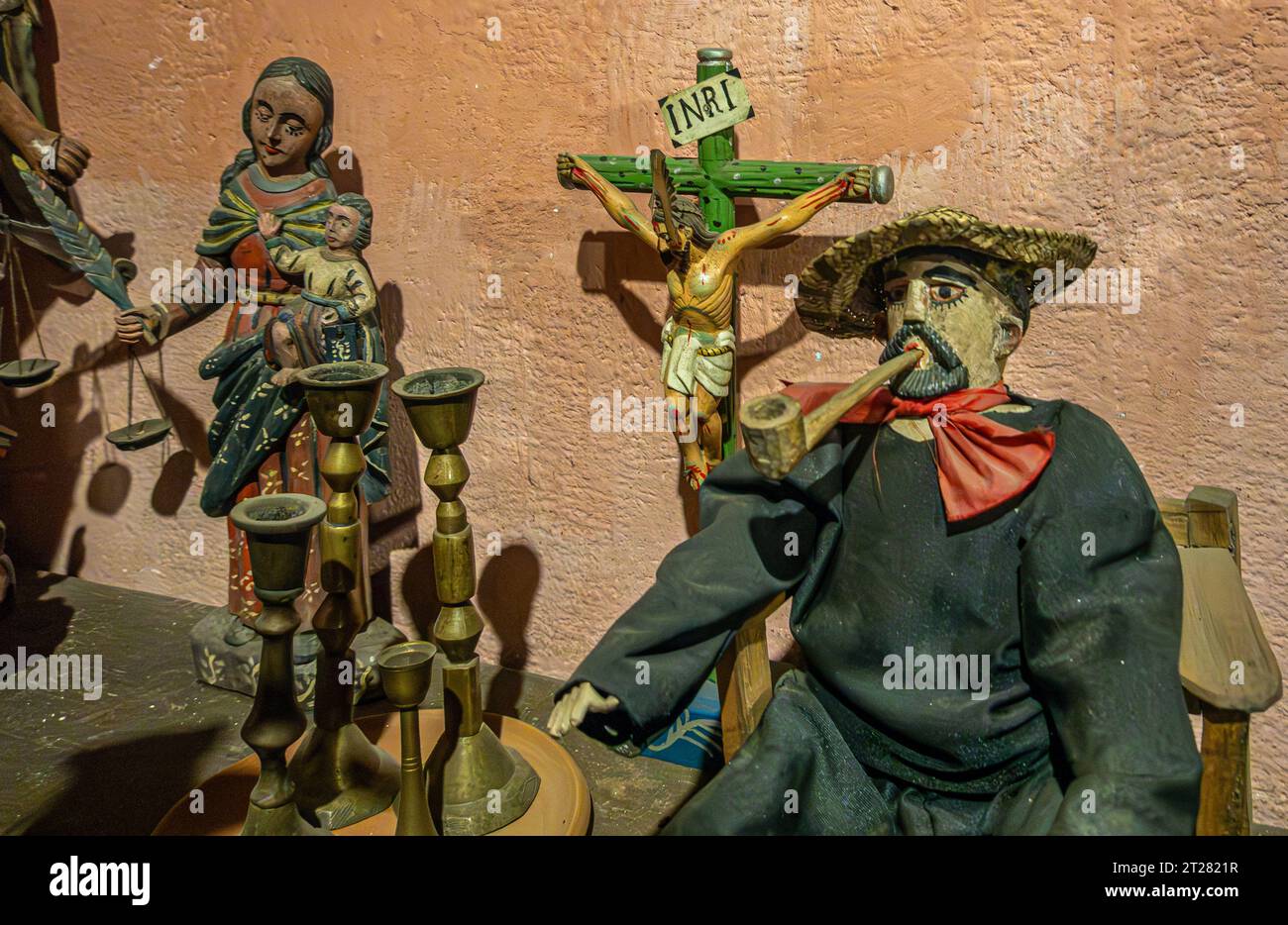 Guatemala, La Antigua - July 20, 2023: Finca La Azotea museums. Pipe smoking man statue with Jesus on cross and mother Mary with baby in back, closeup Stock Photo