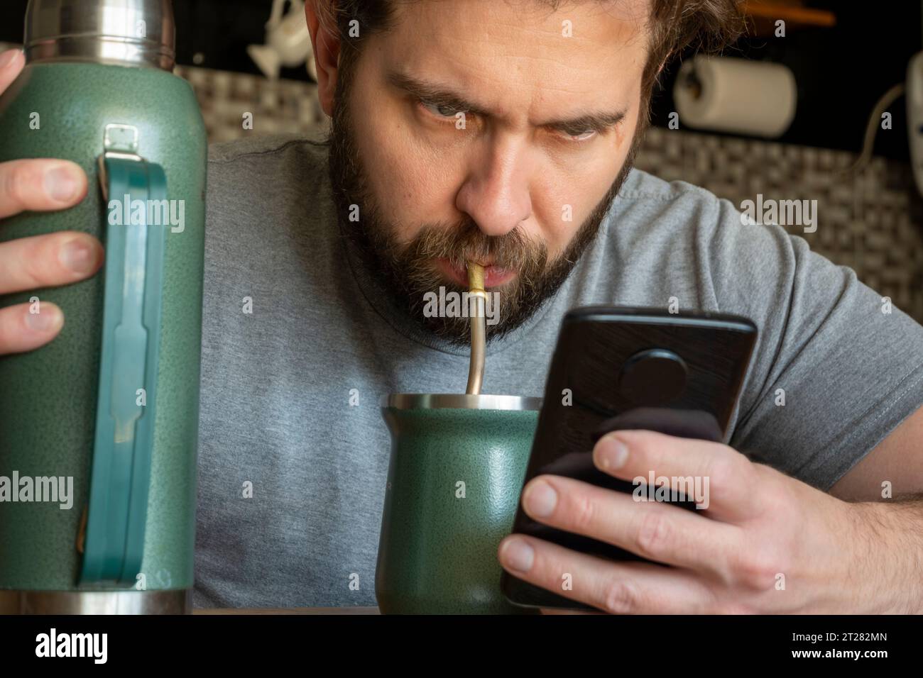 Young Caucasian Latino man drinking mate while checking his phone. Stock Photo