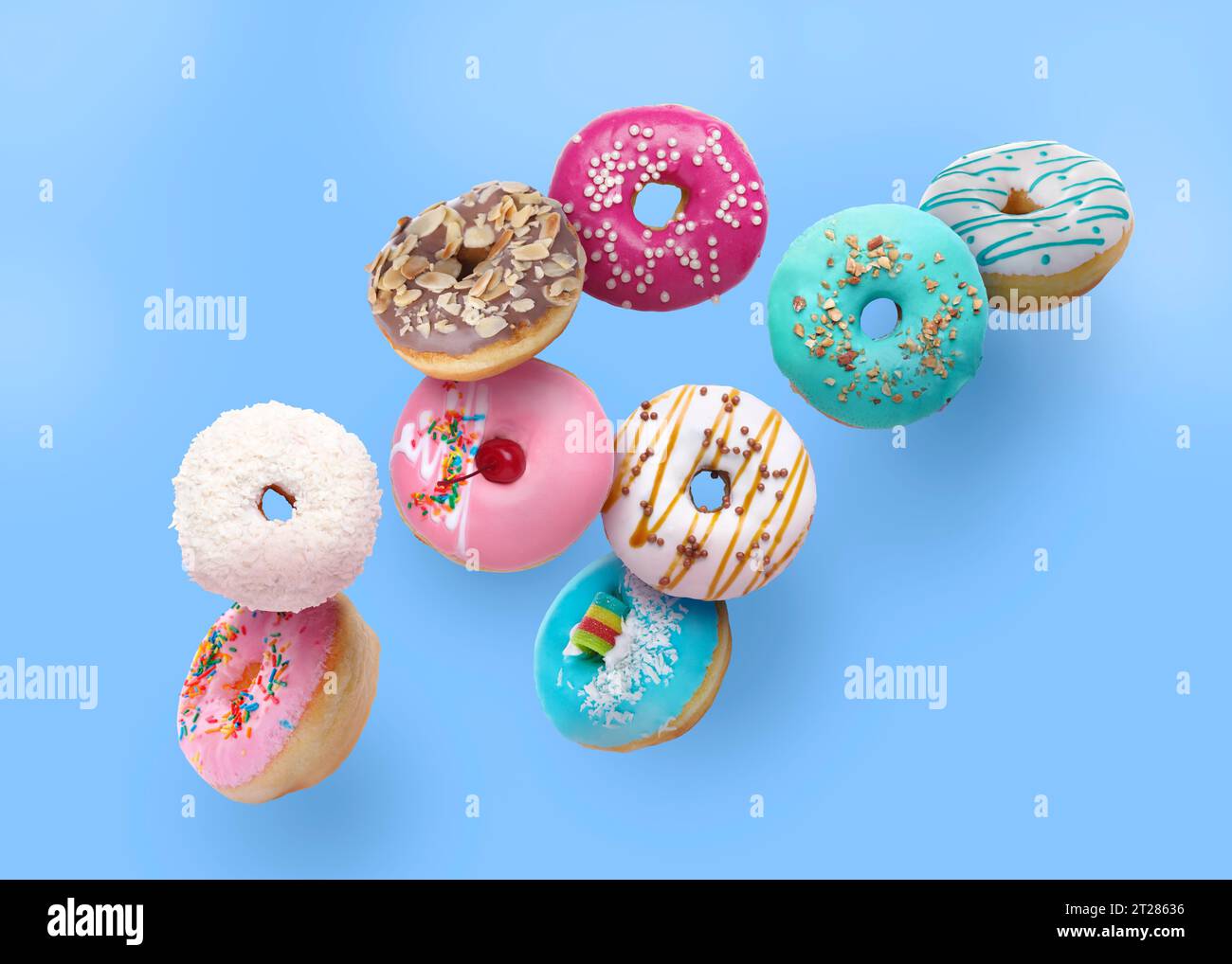 Different tasty donuts falling on light blue background Stock Photo