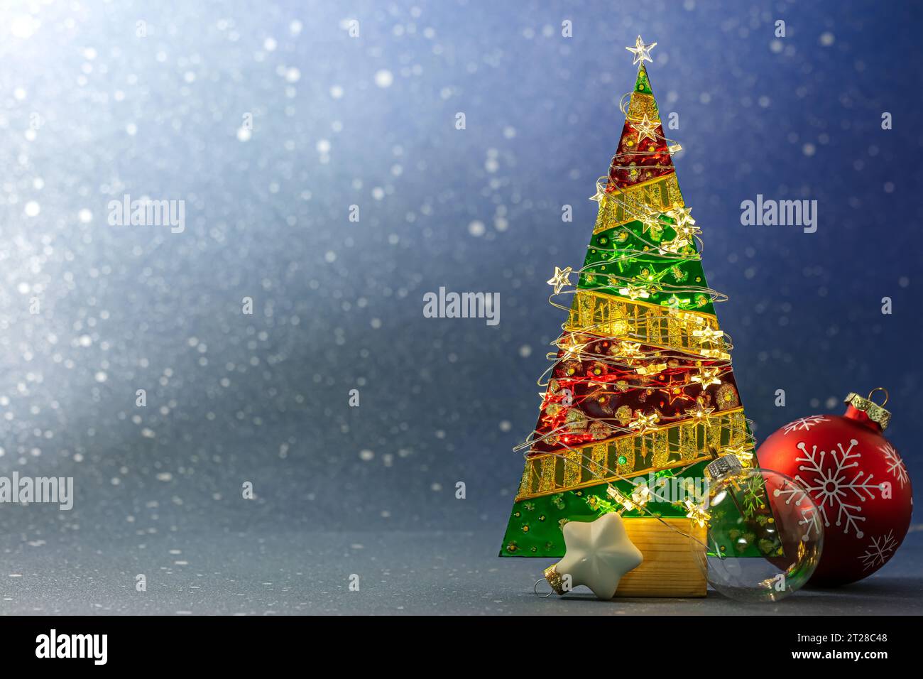 glass christmas tree with festive garland lights and new year balls on blurred blue background. Stock Photo