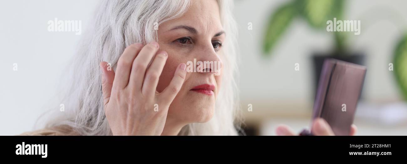 Mature woman with long grey hair examines wrinkles on face Stock Photo ...