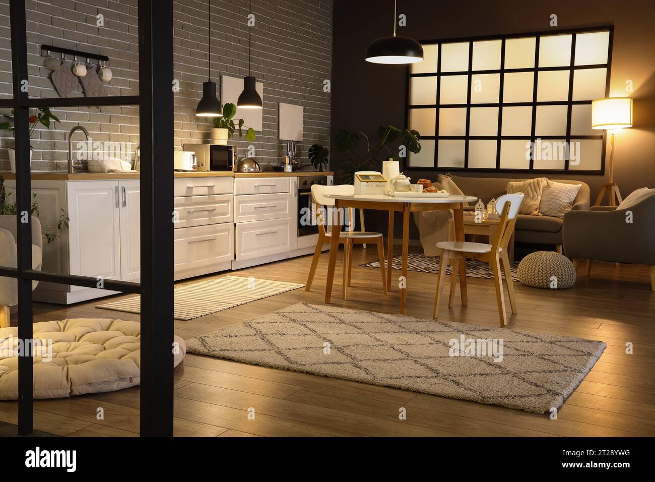 Interior of modern kitchen with glowing lamps, dining table, white ...