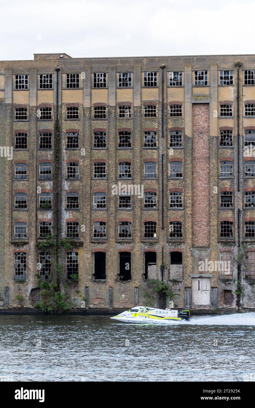 Disused Rank Hovis Premier Mill warehouse on Royal Victoria Dock, Docklands, Newham, London, UK. Built 1904, closed 1980s. Powerboat racing past Stock Photo