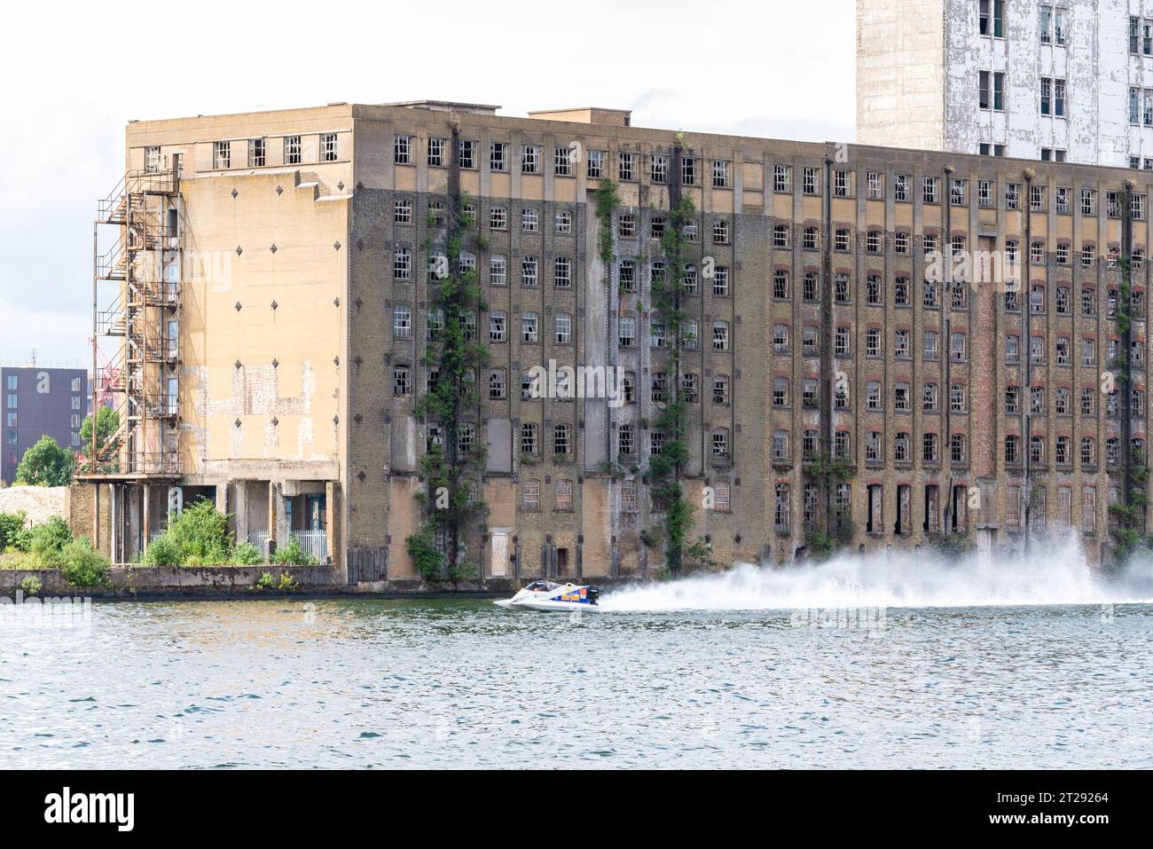 Disused Rank Hovis Premier Mill warehouse on Royal Victoria Dock, Docklands, Newham, London, UK. Built 1904, closed 1980s. Powerboat racing past Stock Photo