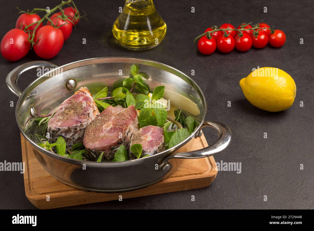 Fresh river fish and mint in pan. Cherry tomatoes, oil and lemon on table. Healthy nutrition. Black background. Top view Stock Photo