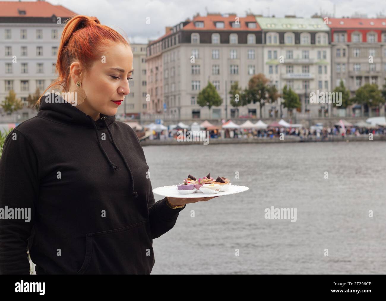 A pretty young woman, a stallholder at a Prague street market, showing off her wares, delicious cheesecake desserts. Stock Photo