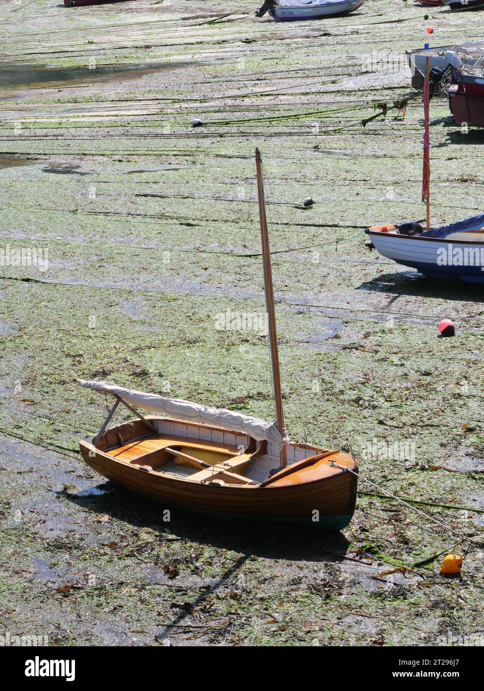 A wooden sailboat lies at low tide on the sandy bottom of the harbor in Mousehole in Cornwall England Stock Photo