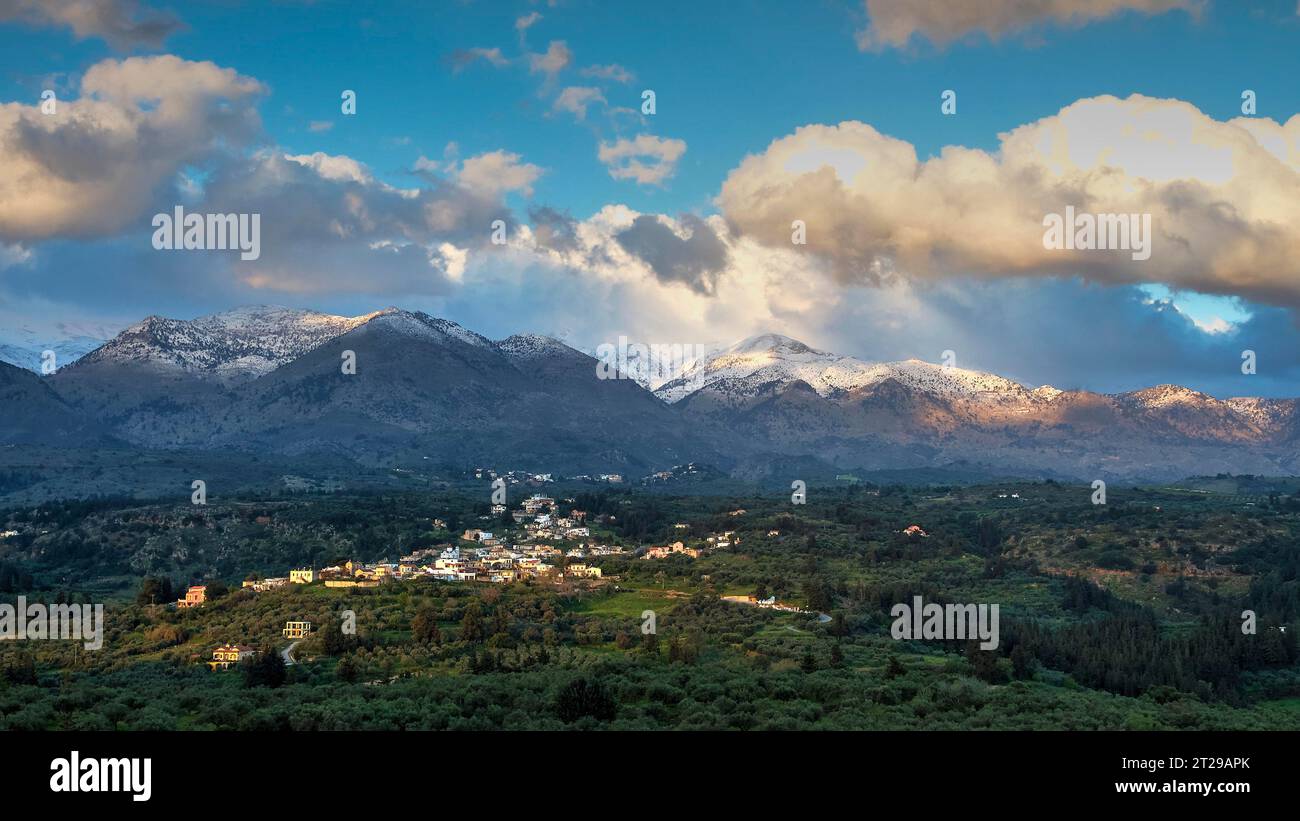 White mountains in morning light, Lefka Ori, snow-capped mountains, village, olive groves, cloudy blue sky, Chania province, Crete, Greece Stock Photo