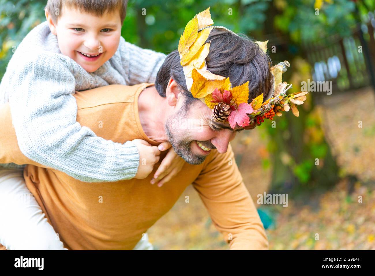 7 October 2023: Dad and son playing in the garden in autumn. Little boy piggybacking on the back of his father with an autumn homemade crown of colorful leaves. Family in autumn concept *** Papa und Sohn spielen im Herbst im Garten. Kleiner Junge Huckepack auf dem Rücken von seinem Vater mit einer herbstlichen selbstgebastelten Krone aus bunten Blättern. Familie im Herbst Konzept Credit: Imago/Alamy Live News Stock Photo