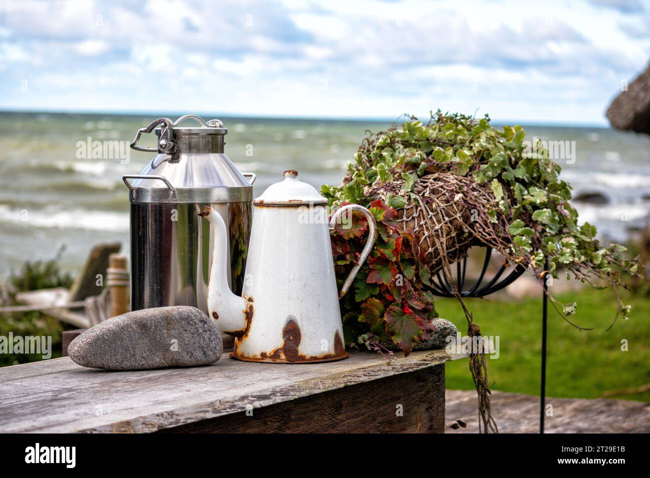 Composition with milk jug tea pot and stone on wooden table with sea background Stock Photo