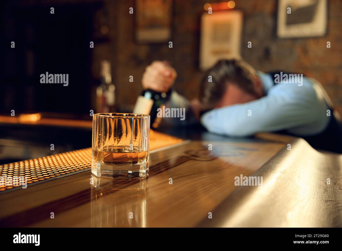 Drunk man sleeping at bar counter with focus on alcoholic drink in