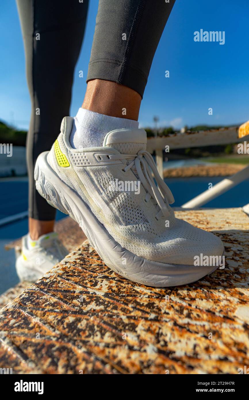 Close-up detail of the white running shoes of an athletic woman climbing some rusty iron stairs to strengthen the glutes and quadriceps on a sunny day Stock Photo